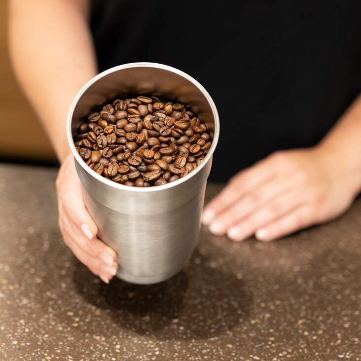 Hand hält Becher voller Kaffeebohnen