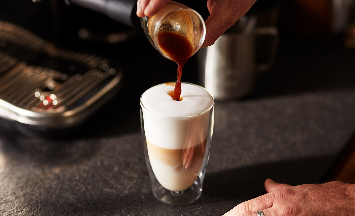 Hand gießt Espresso in Milchschaumglas
