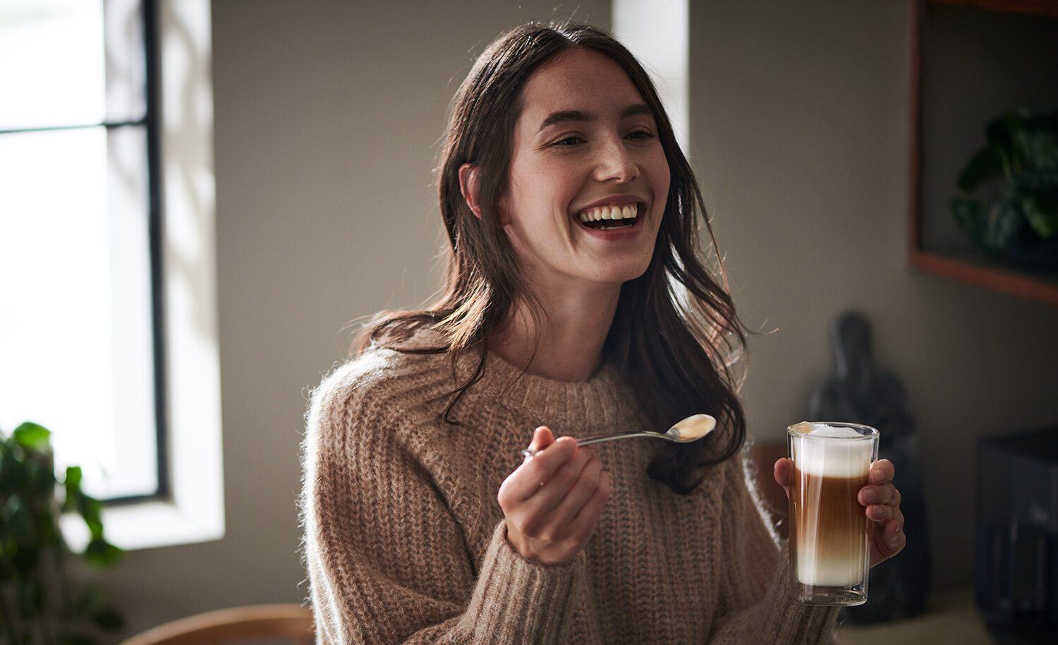 Person mit Latte Macchiato und Löffel in der Hand