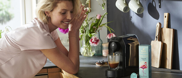 Frau in Küche neben Kapselmaschine und Kaffee