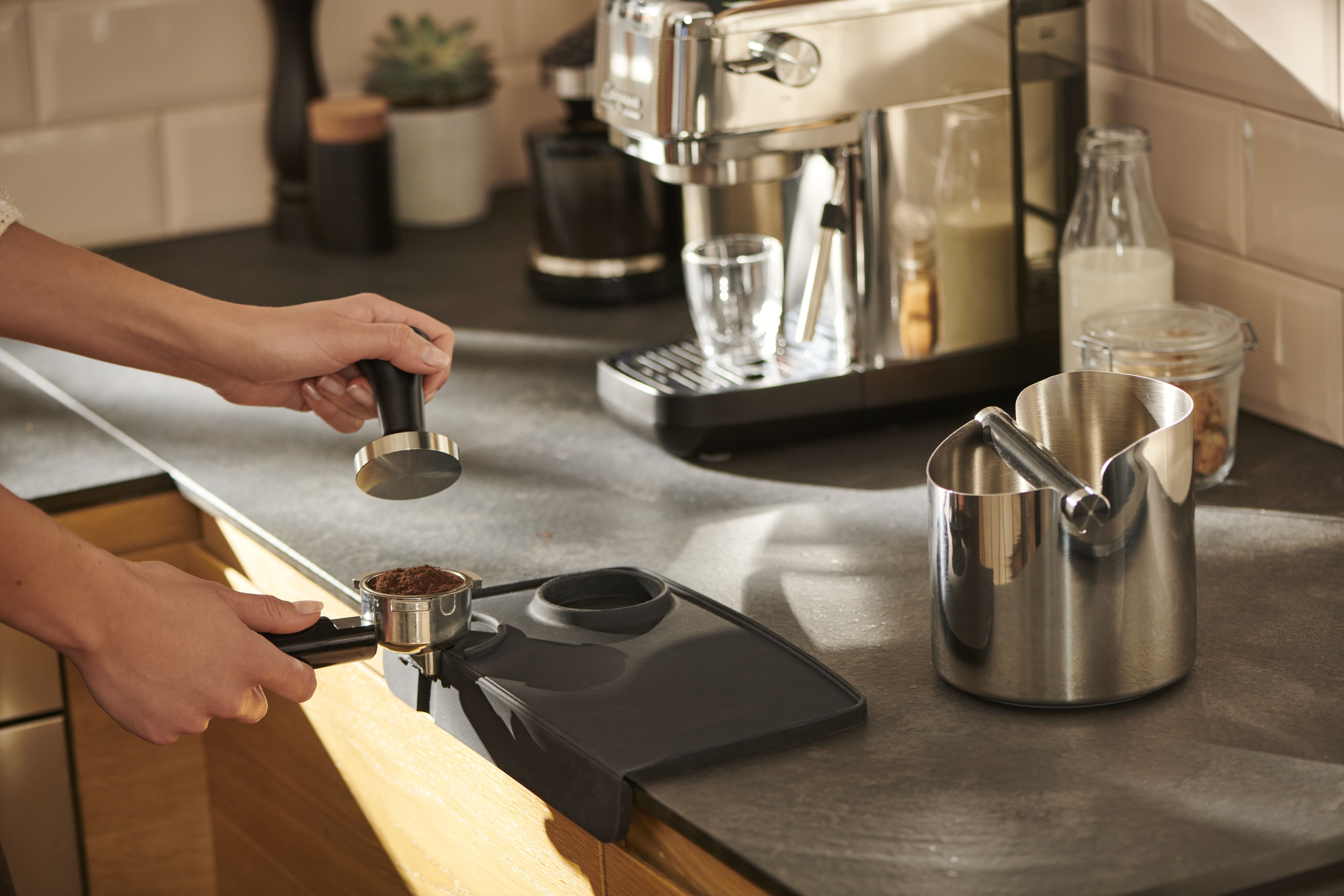 Hände tampern Kaffeepulver an Espressomaschine