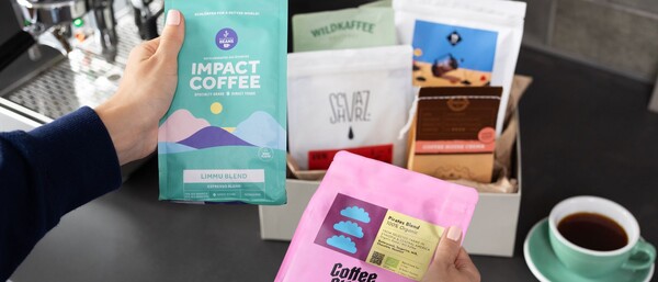 Hände halten bunte Kaffeepackungen vor Espressomaschine