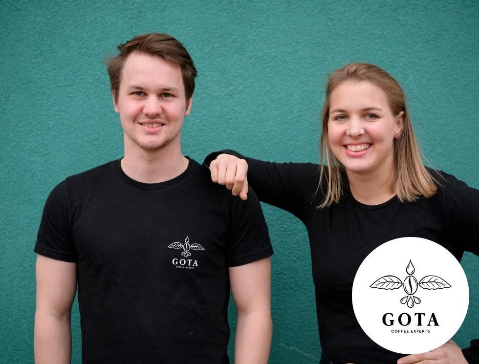 Zwei Personen in GOTA-T-Shirts vor türkiser Wand