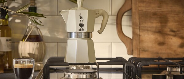 Cremefarbige Espressokanne auf Gasherd mit Glas Espresso