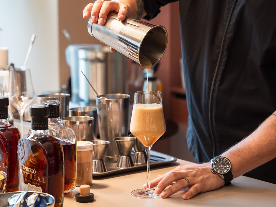 Barkeeper gießt cremigen Cocktail ins Weinglas