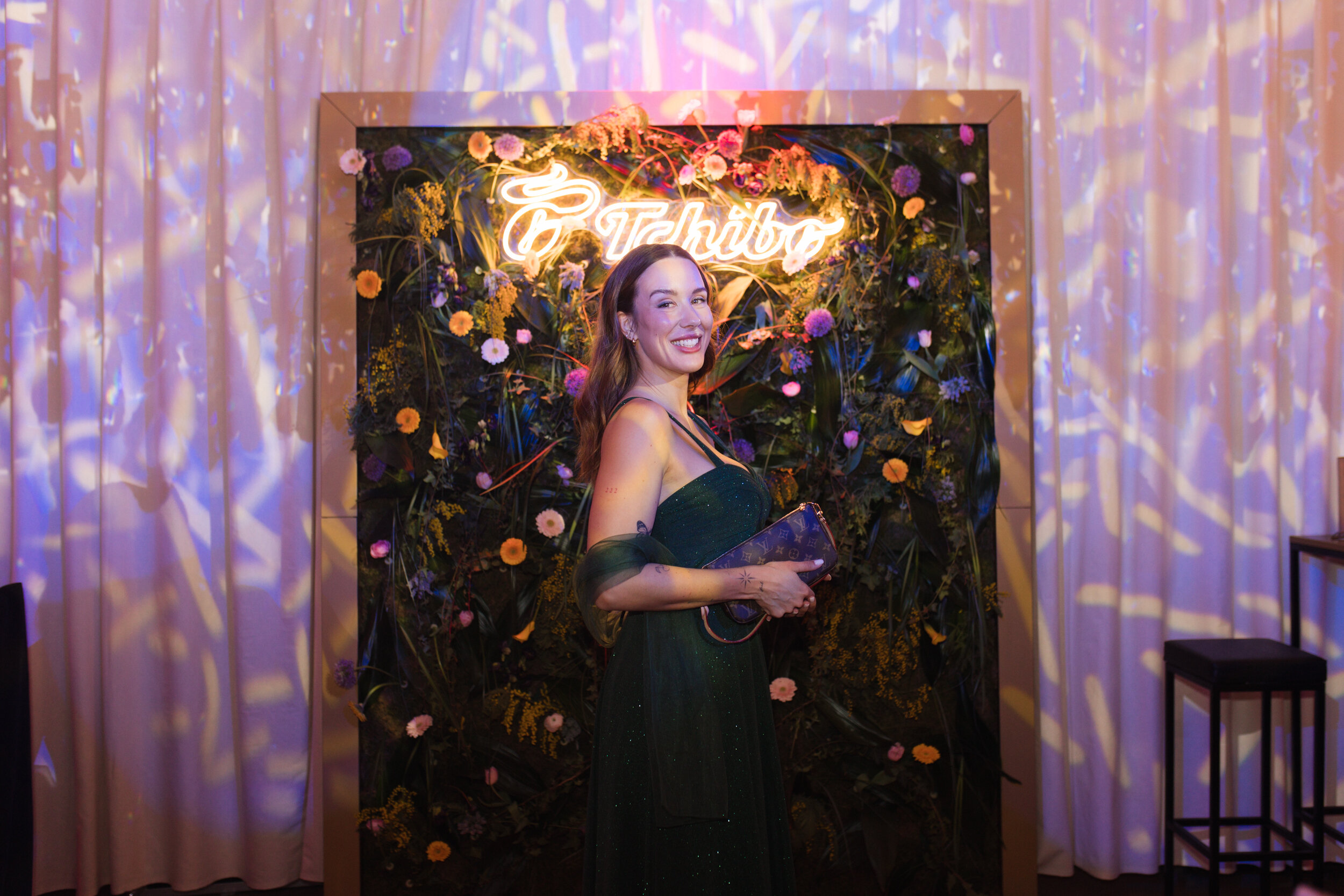 Frau im Abendkleid vor beleuchteter Blumenwand