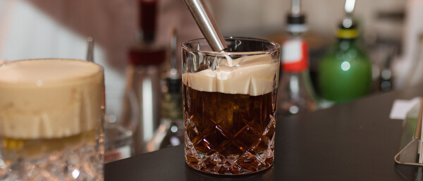 Hand schenkt Schaum auf dunklen Cocktail in Glas