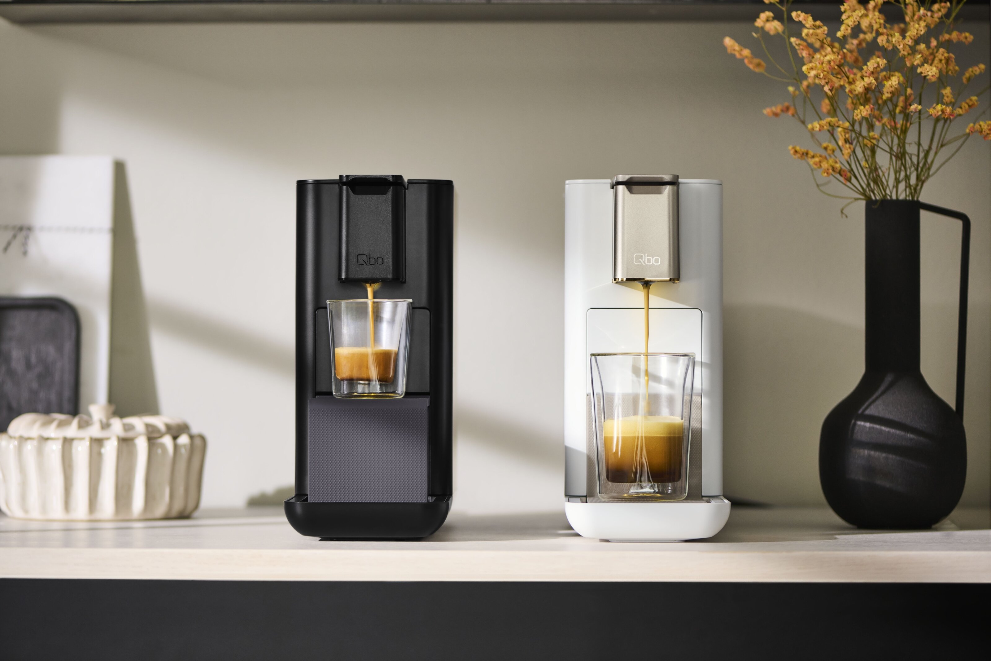 Zwei Qbo-Kaffeemaschinen mit Espresso-Tassen