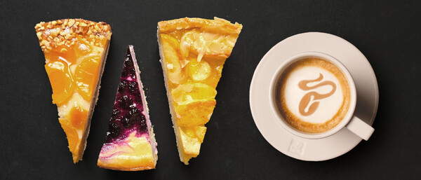 Drei Kuchenstücke und Cappuccino auf schwarzem Tisch