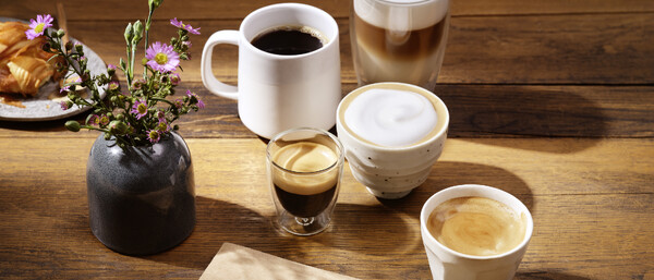 Mehrere Kaffees, Notizbuch, Blumen und Gebäck