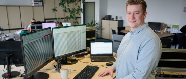 Person im Großraumbüro vor zwei Monitoren