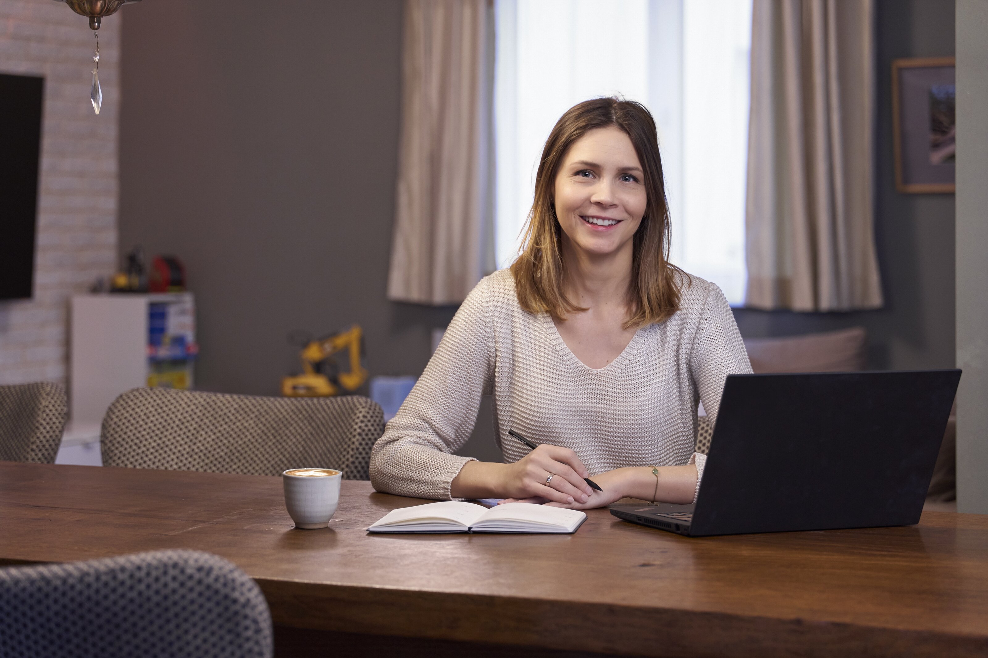 Frau am Tisch mit Laptop, Notizbuch und Kaffee