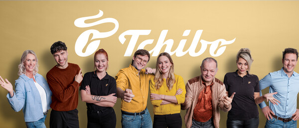 Gruppe Menschen vor Tchibo-Logo auf gelbem Hintergrund
