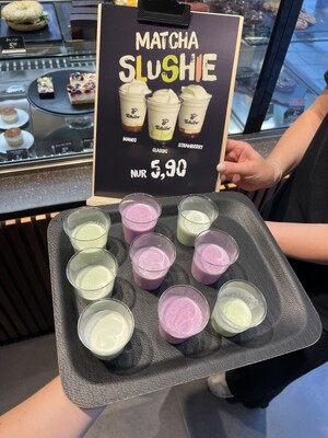 Link: Großansicht des Bildes - Bildinhalt: Tablett mit Matcha-Slushie-Proben vor Werbeschild