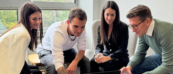 Vier Personen schauen gemeinsam auf einen Laptop