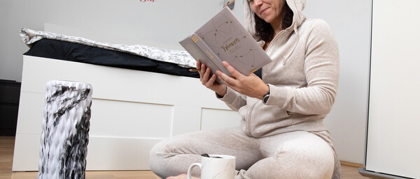 Frau im Jogginganzug liest sitzend auf Yogamatte