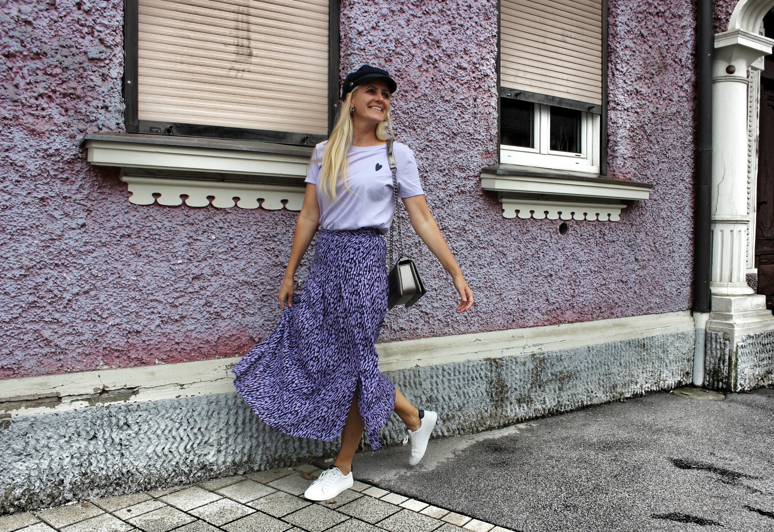 Frau in lila Outfit vor rauer Hauswand