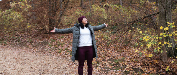 Person mit ausgebreiteten Armen im herbstlichen Wald