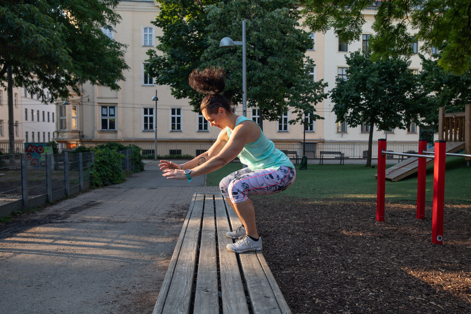 Frau macht Sprungübung auf Holzbank im Park