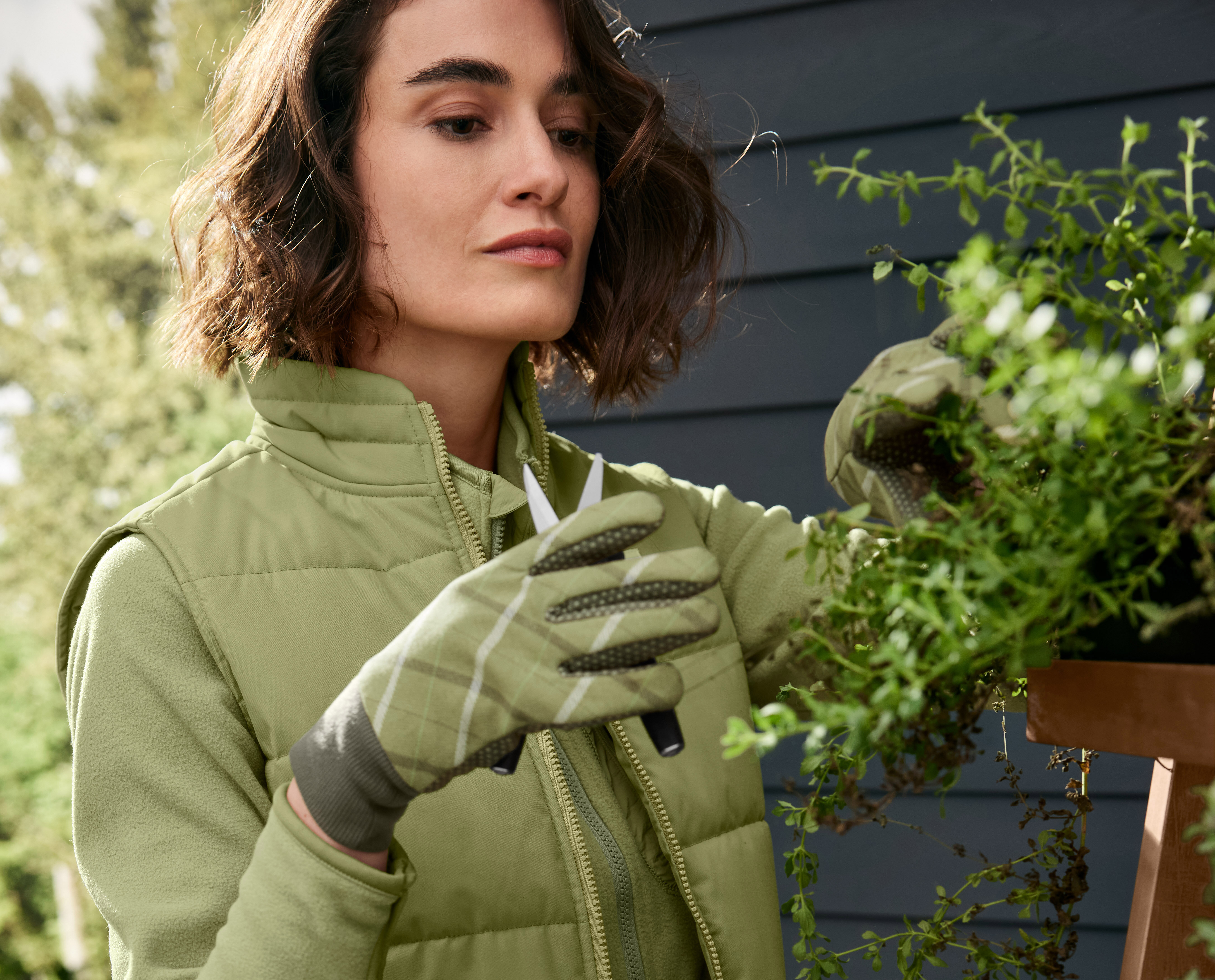 Frau mit Gartenhandschuhen schneidet Kräuter