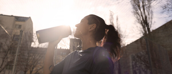 Sportlerin trinkt im Sonnenlicht aus Flasche