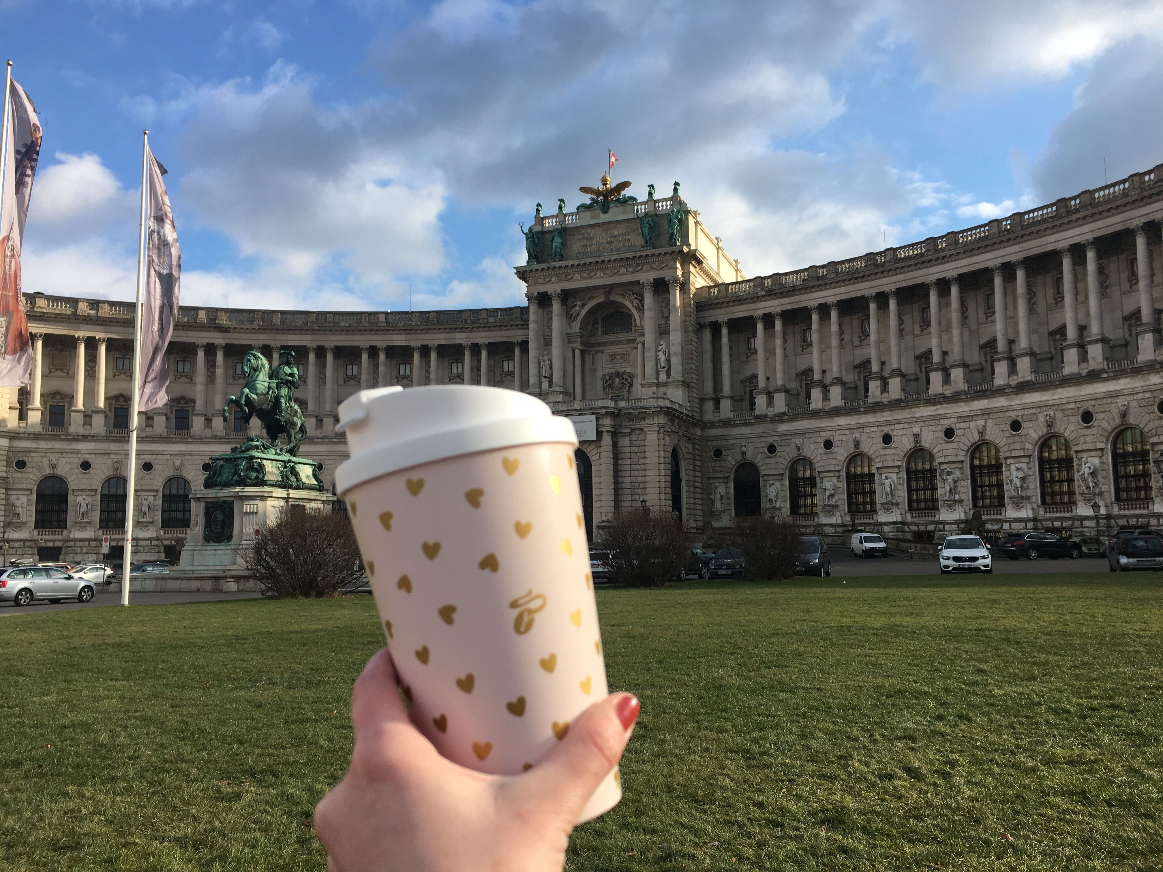 Hand hält Kaffeebecher vor historischem Gebäude