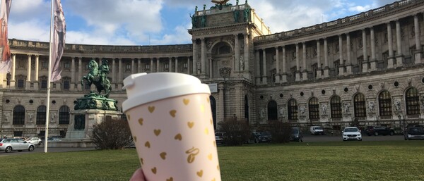 Hand hält Kaffeebecher vor historischem Gebäude