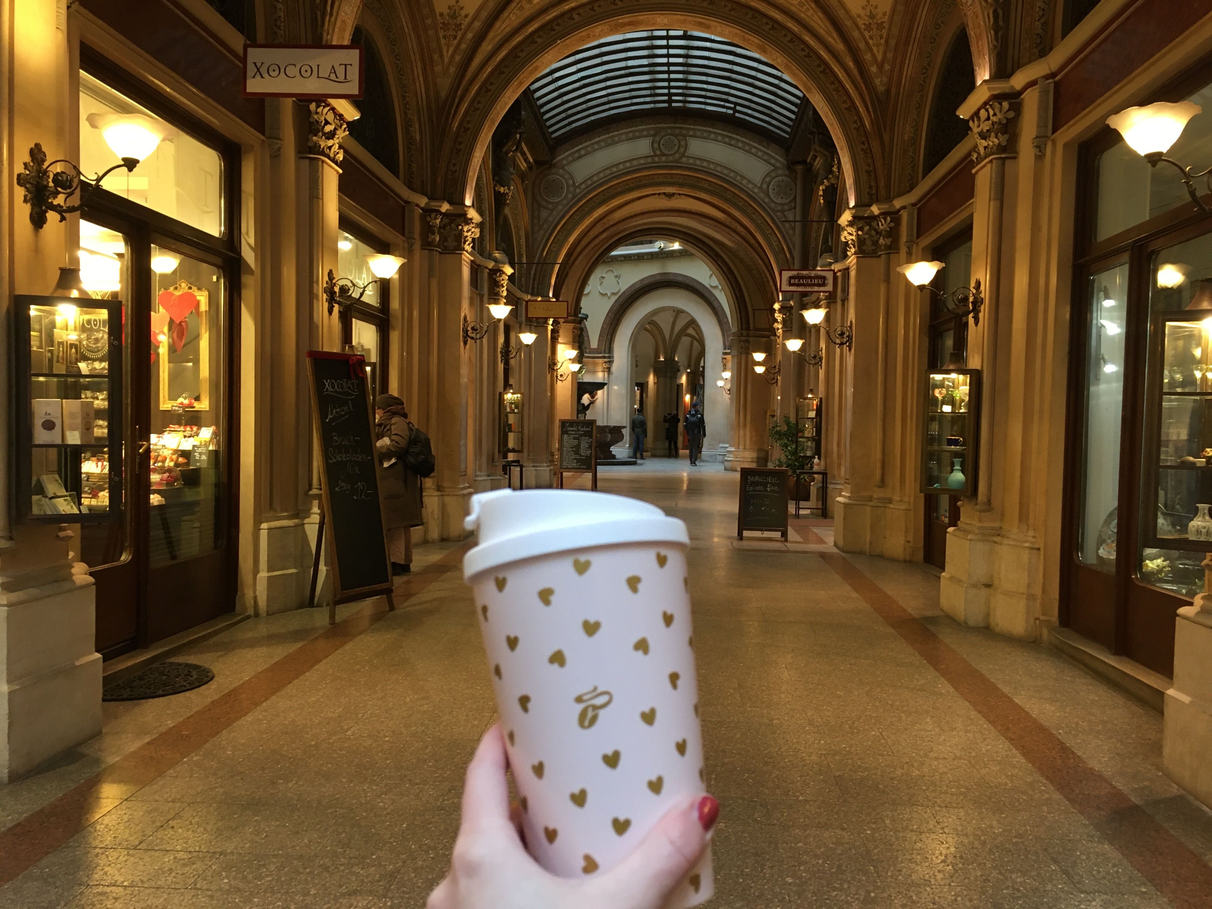 Hand mit Kaffeebecher in eleganter Ladenpassage