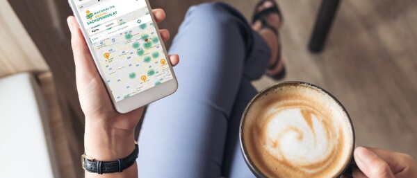 Handy mit Karten-App und Cappuccino in der Hand