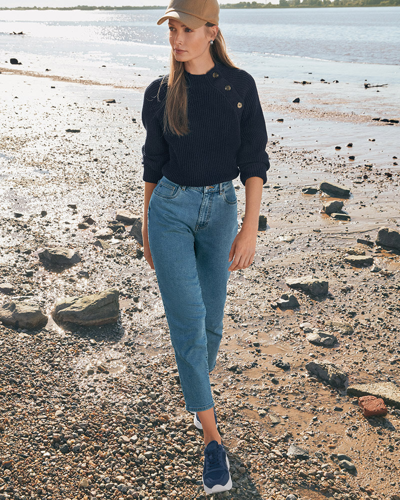 Frau in Jeans und Pullover spaziert am Kiesstrand