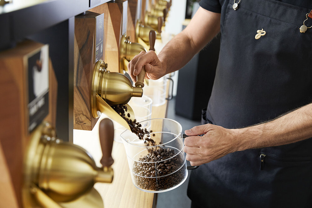 Mitarbeiter füllt Kaffeebohnen aus goldenen Spendern
