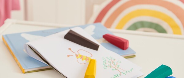 Kinderzeichnung mit bunten Wachsmalstiften auf Tisch