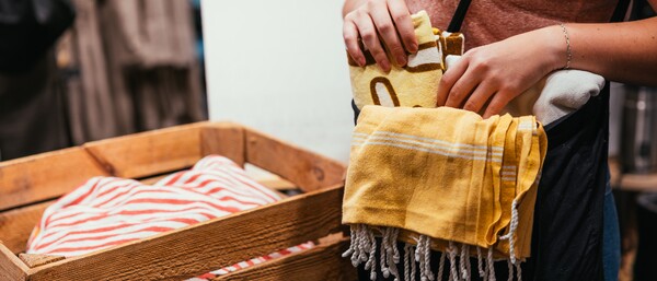 Person steckt gelbes Handtuch in Tasche neben Holzkiste