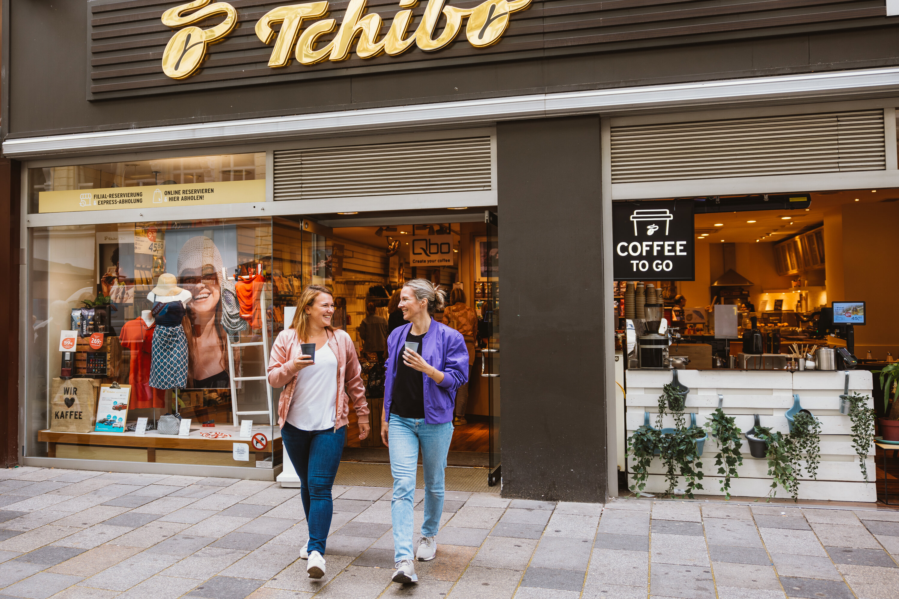 Zwei Personen mit Coffee-to-go vor Tchibo-Filiale