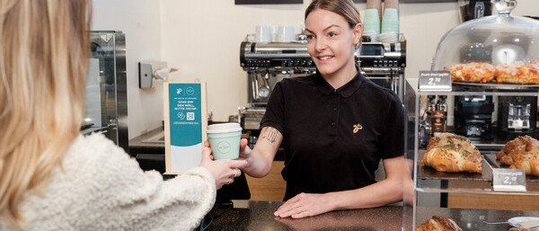 Barista reicht Kundin Kaffee an Bäckereitheke