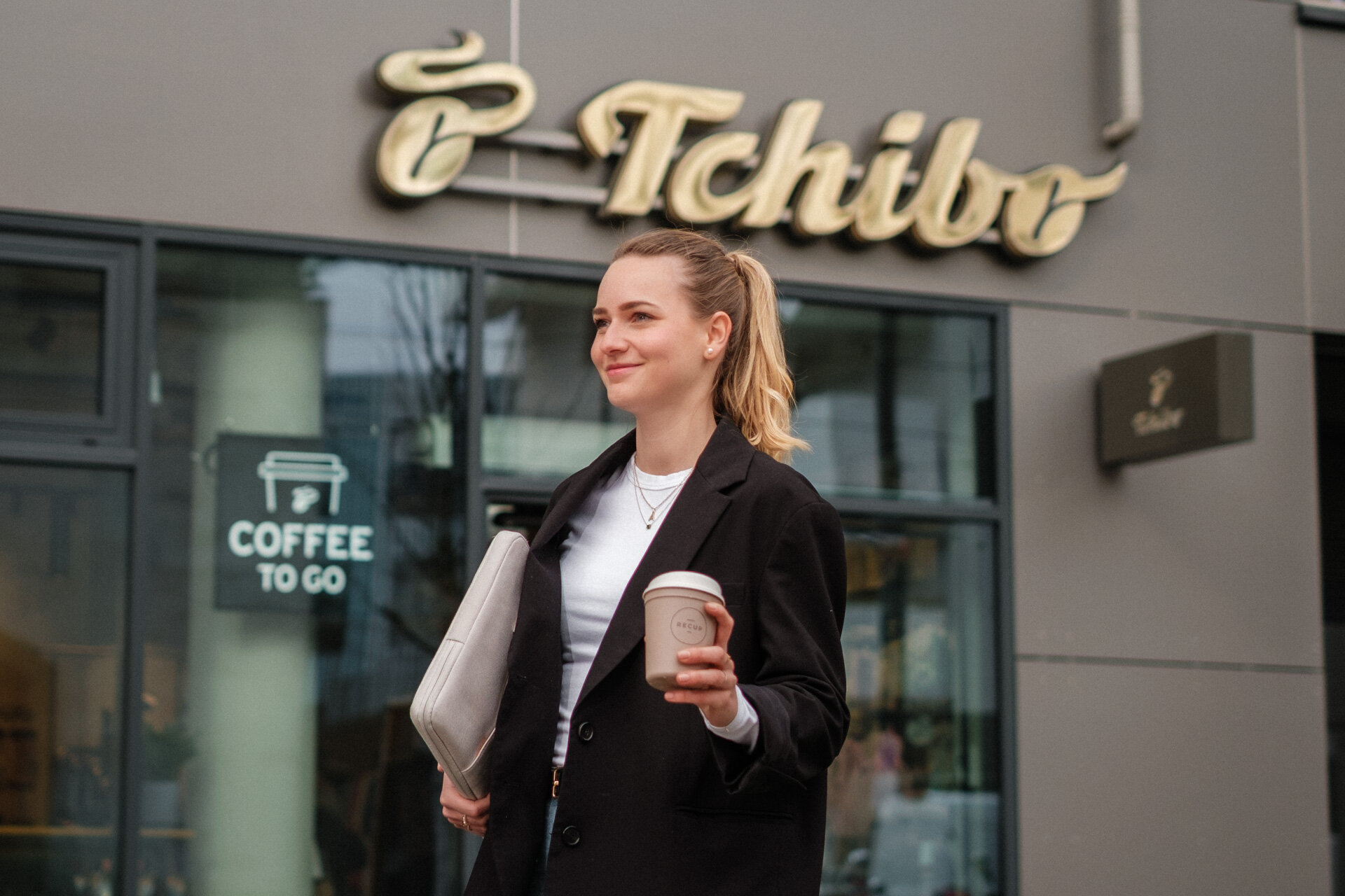 Frau mit Kaffeebecher vor Tchibo-Filiale