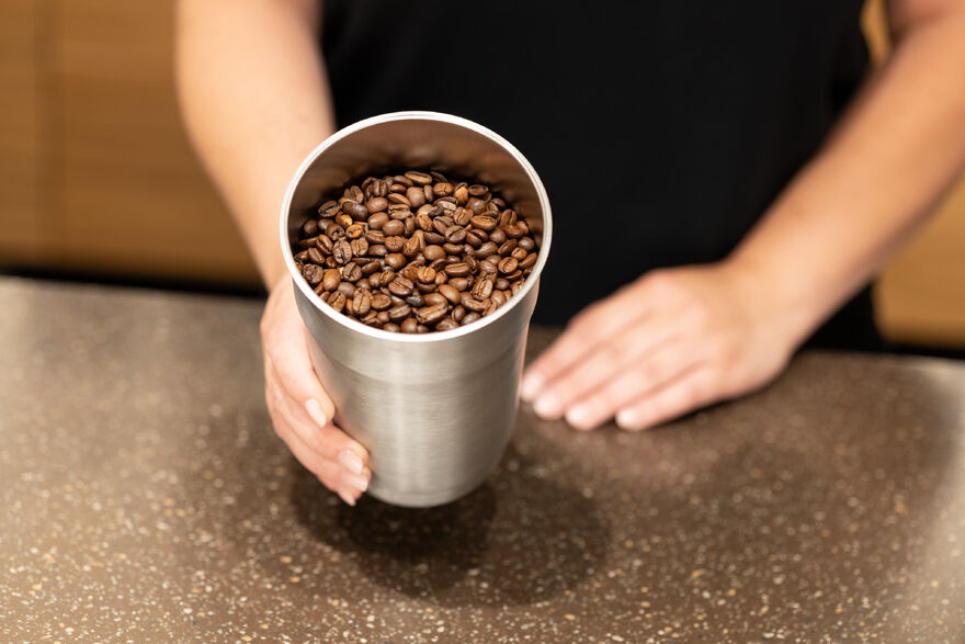 Hand hält Becher voller Kaffeebohnen