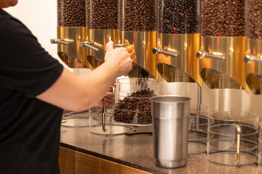 Person füllt Kaffeebohnen aus goldenen Spendern
