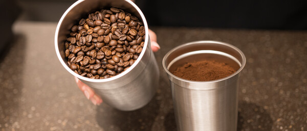Hand hält Becher mit Bohnen neben gemahlenem Kaffee