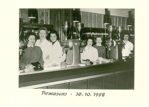 Link: Großansicht des Bildes - Bildinhalt: Schwarz-weiß-Fotografie aus dem Jahr 1958 mit einer Gruppe von Tchibo Mitarbeiterinnen hinter einer langen Theke. Auf der Theke stehen drei große Kaffeemühlen. Unten im Bildrand handschriftlich vermerkt: „Pirmasens · 30.10.1958“.