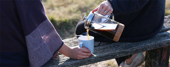 Person schenkt Kaffee in weiße Tasse draußen
