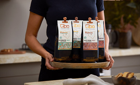Person hält Tablett mit vier Qbo-Kaffeepackungen