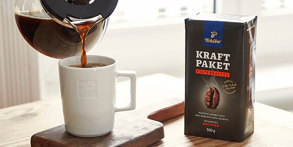 Kaffee wird in Tasse neben Tchibo-Kaffeepackung gegossen