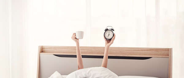 Arme ragen aus Bett, halten Tasse und Wecker