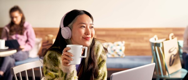 Person mit Kopfhörer trinkt Kaffee vor Laptop in Café