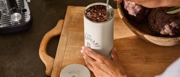Hände öffnen Kaffeedose mit Bohnen neben Espressomaschine