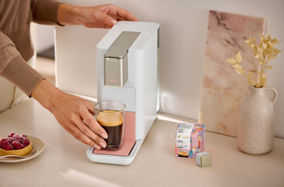 Hand nimmt Glas Kaffee aus moderner Kapselmaschine