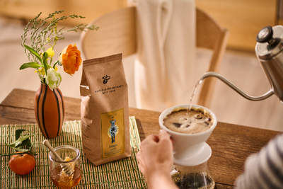Hand gießt Filterkaffee neben Blumen und Honig