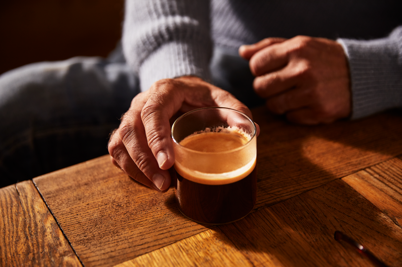 Hand hält Glas Espresso auf Holztisch