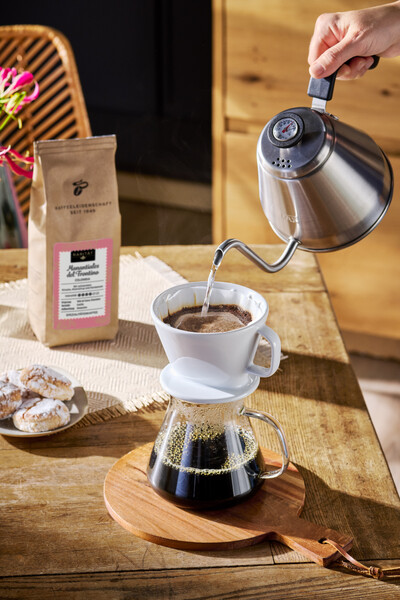 Hand gießt Filterkaffee in Glaskanne auf Holztisch